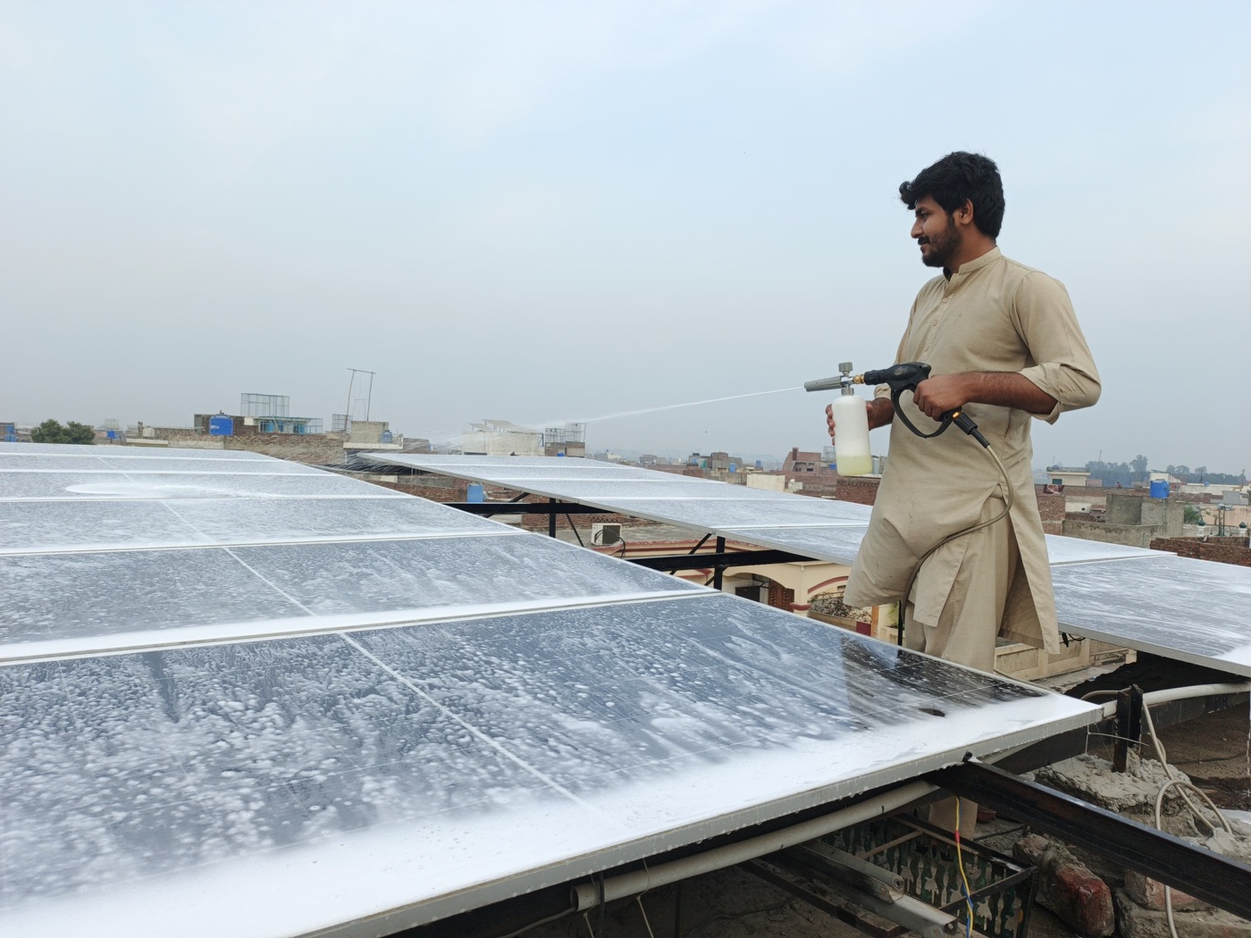 Technician cleaning solar panels with foam spray on a Lahore rooftop